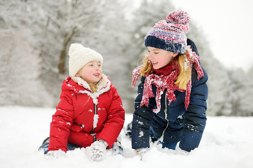 The group of cute happy children dressed in colorful (rainbow palette) winter clothing. They are having fun and playing in a snow together. The different ages children are ranning on a snowdrifts. They are laughing and trying to outrun each other. The outdoors shooting in a sunny frosten day at a winter