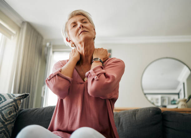 年配の女性、脊椎損傷、線維筋痛症、骨粗鬆症の居間の家で首の痛みとストレス。整形外科、関節炎、健康上の問題の病気の、疲れた、疲れた女性の筋肉を伸ばす - arthritis osteoporosis pain backache ストックフォトと画像