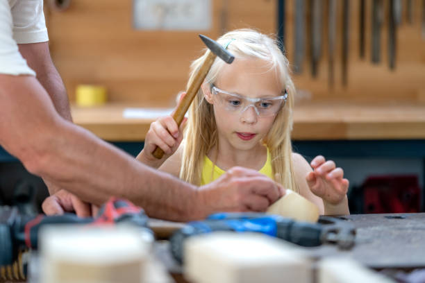 Girl wearing protective glasses using hammer in handcraft class, front view Girl wearing protective glasses using hammer in handcraft class, front view. Kid making wooden toy in carpentry workshop, medium shot girl with a hammer stock pictures, royalty-free photos & images