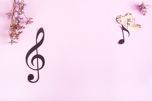Paper musical clef, notes, hearts and dried flowers on a pink background. Top view.