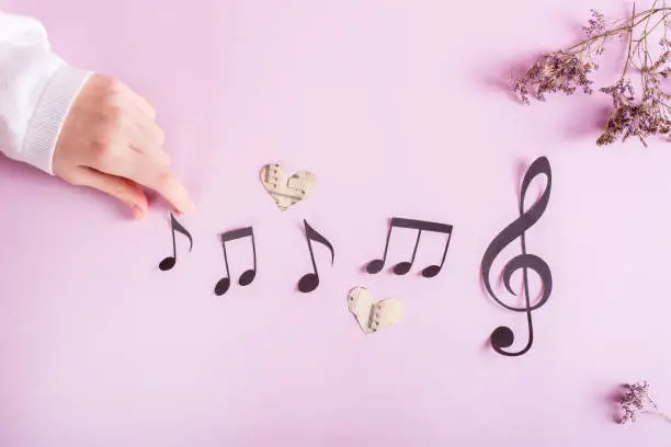 Paper musical clef, paper notes and children's hand on pink. Music education. Top view.
