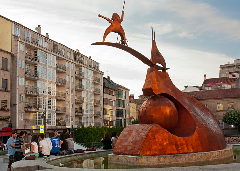 Carballino, Spain-July 7,2011: Town square view in O Carballiño, Ourense province, migrants  monument, residential building facades, sidewalk cafes, pedestrian zone. People sitting, walking,talking.