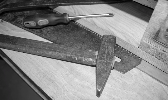 Home repair tools on wooden slats. On a wooden pallet is a hammer, a screwdriver and a saw - black and white photo.