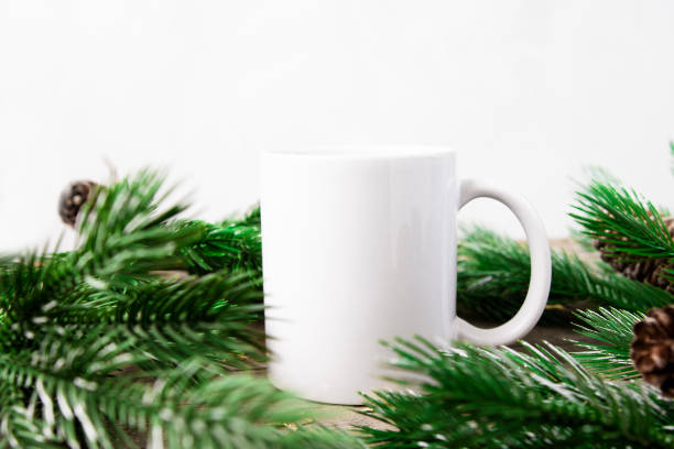 istock White cup with empty copy space on a white background with green Christmas tree branches. Template for applying text and drawing, front view. 1445339498