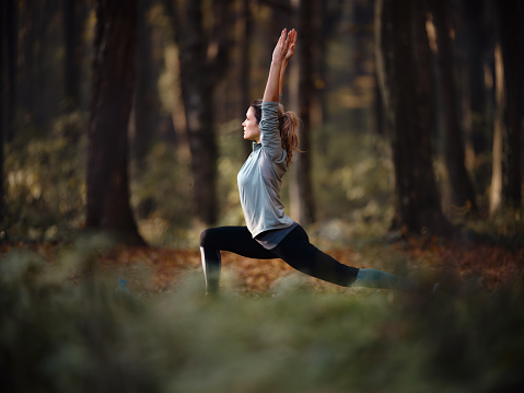 Young athletic woman doing stretching exercises with raised arms during a Pilates training in autumn day, Copy space.