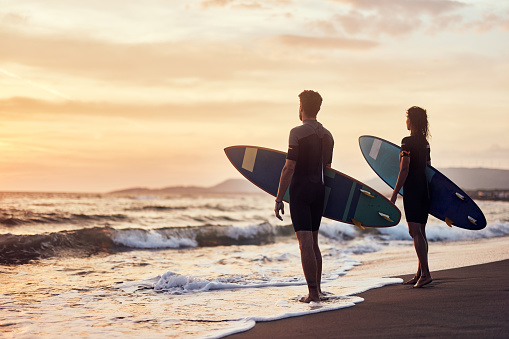 Couple of surfers with their surfboards during summer sunset on the beach. Copy space.