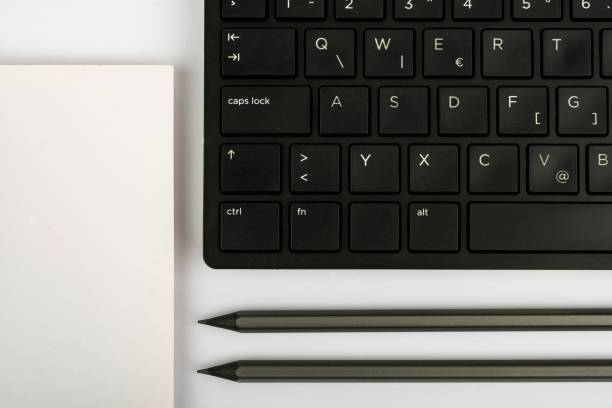 A closeup of a computer keyboard with office stationery on a white background