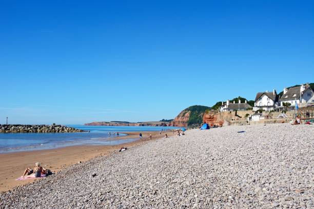 Tourists relaxing on the beach with cottages overlooking the sea, Sidmouth, Devon, UK, Europe.
