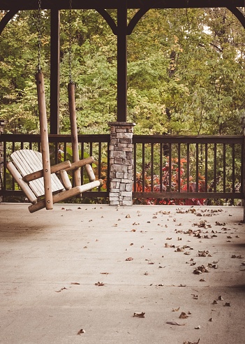 A vertical shot of a wooden swinging chair amongst autumn leaves on a veranda in Tennessee, USA