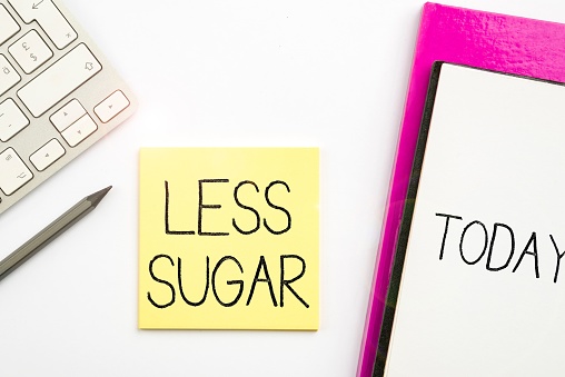 A LESS SUGAR text written on a notepad surrounded with some office supplies
