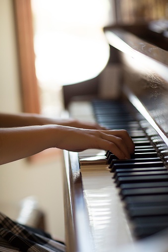 A vertical selective focus shot of the experienced hands of a professional playing the piano indoors