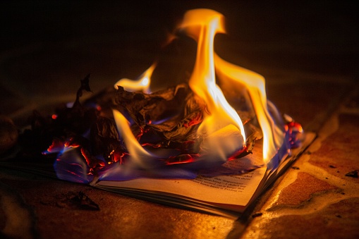 The burning paper, open book burns to ashes on concrete tiles, manuscript burns in outside