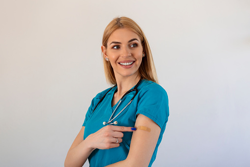Young woman doctor with adhesive bandage on her arm after Coronavirus vaccine. First aid. Medical, pharmacy and healthcare concept.
