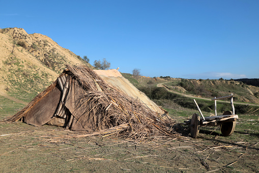 A reed tent on a mountain slope. There are old furniture and fire in front of the tent.