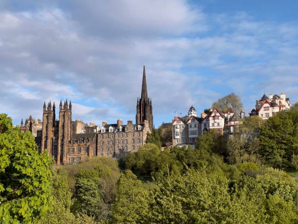 istock Old buildings in Edinburgh behind lush green trees on blue cloudy sky background 1445367201