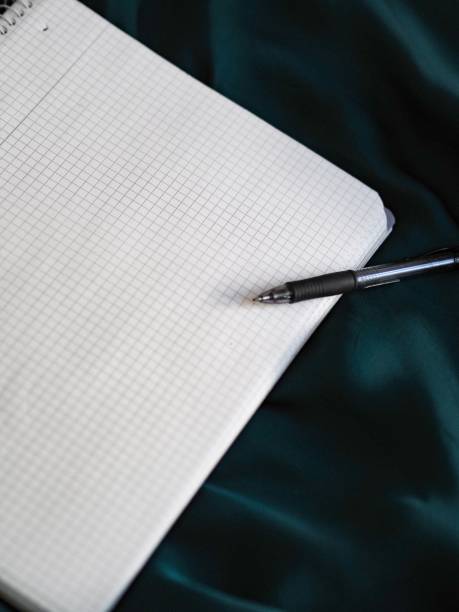istock Pen and graphing paper on a shiny blue fabric surface, vertical shot 1445367562