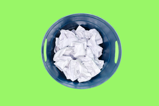 istock Plastic trash can being filled with crumpled sheets of white paper, isolated on a green background 1445374414