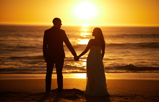 Love, summer and couple silhouette at a beach at sunset, holding hands and bonding with ocean views in nature. Romance, travel and nature with man and woman enjoying sea honeymoon and romantic trip