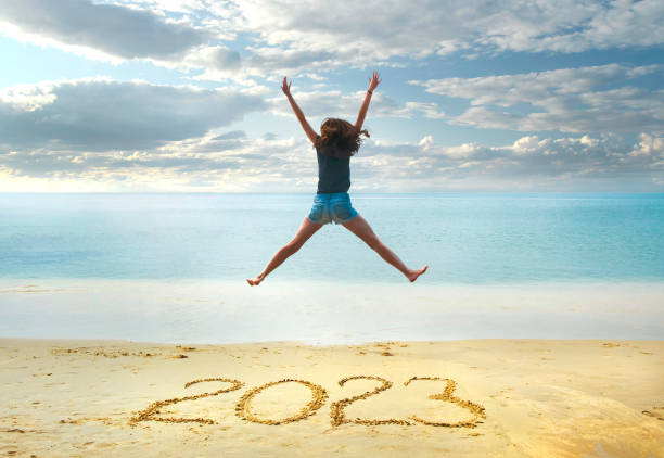 capodanno 2023 scritto sulla sabbia, giovane donna felice con le mani alzate che salta sulla spiaggia - beach women joy sand foto e immagini stock