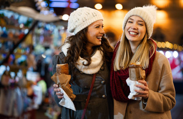 glückliche menschen, die sich gemeinsam auf einem festlichen weihnachtsmarkt auten. weihnachtsferien-people-konzept - people eating walking fun stock-fotos und bilder