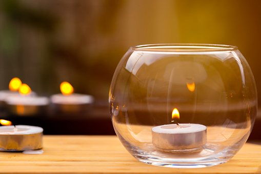 Candle light in clear glass jar on wooden table background.