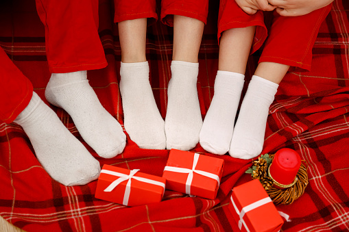 Feet in wool socks near Christmas tree in winter time. Mother, father and children having fun in Christmas time. Man, woman and kid relaxing at home. Winter holiday Xmas and New Year concept