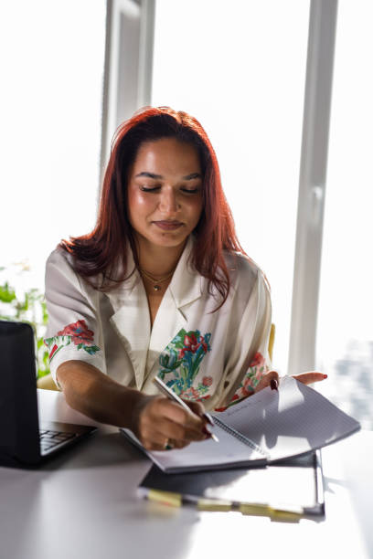 istock Smiling young woman writing notes at her desk while working 1445379669