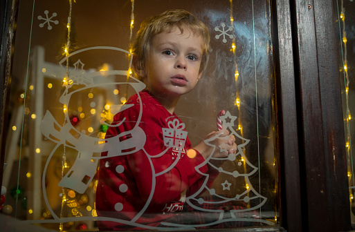 Little excited child is waiting Santa Claus on Christmas Eve. Preschooler boy looking on window and hope of magic and gifts at New Year night