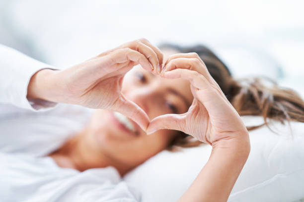 istock Young nice woman on the bed showing heart 1445381245