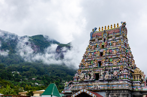 Arul Mihu Navasakthi Vinayagar Temple with colorful traditional Hindu gods and deities sculptures and tropical mountains in clouds in the background, Victoria, Mahe Island, Seychelles.