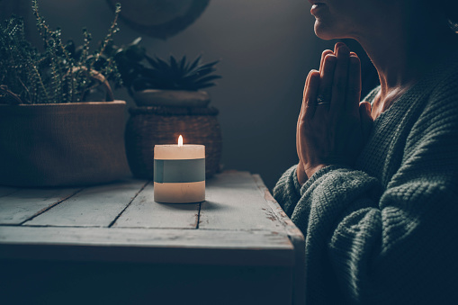 Zen like lifestyle meditation in front of a candle light praying for one woman at home. Green mood color style. Mental health concept. Faith and religion. Candlelight in the dark indoor. Female people