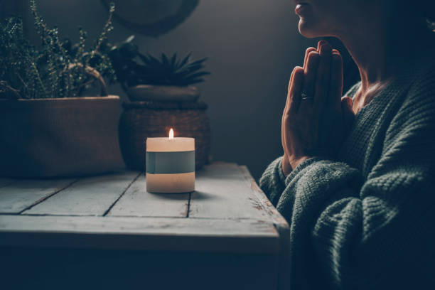 Zen like lifestyle meditation in front of a candle light praying for one woman at home. Green mood color style. Mental health concept. Faith and religion. Candlelight in the dark indoor. Female people stock photo