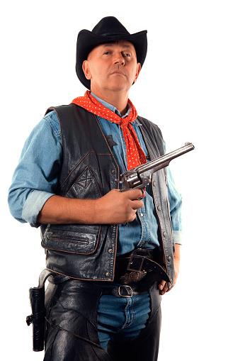 Cowboy holds up a revolver in one hand standing in front of the white background