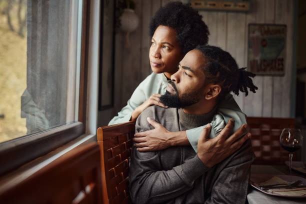 Pensive black couple looking through window from home.
