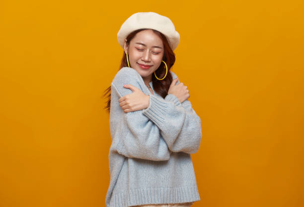beautiful Asian teenager woman hugging and embracing herself isolated on studio yellow background. selflove appreciation and self care concept. stock photo