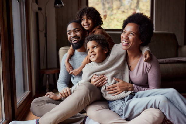 Happy black family enjoying in their time at home. Happy African American parents and their small kids spending time together in the living room. looking through window photos stock pictures, royalty-free photos & images