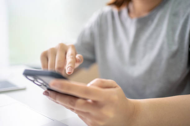 istock Hands of young woman pointing at smartphone screen over laptop keypad while using mobile gadgets at work 1445389215