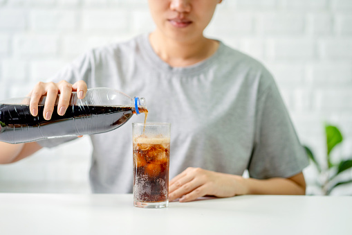 Woman pouring of cola into a glass with ice.