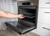 Modern electric oven with telescopic rails and steel baking tray. Hinged oven door. Black oven in a white kitchen. Automatic cooking program