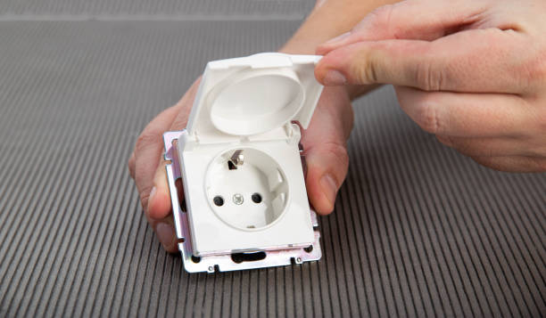 istock A man's hand holds an electric switch with a protective cover on a gray background, close-up. Splash and rain resistant outdoor socket, close-up 1445391421