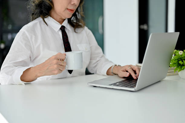 istock cropped image, Professional Asian aged female manager sipping coffee while using laptop 1445391521