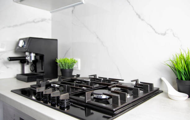 istock Modern kitchen with gas hob against white granite tiles. Decoration pots with artificial flowers. Copy space for text 1445391700