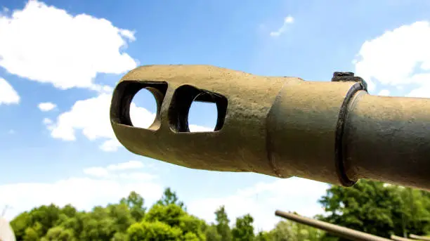 Photo of The muzzle of a cannon of a military tank against the blue sky, close-up. The concept of military conflict, aggression.