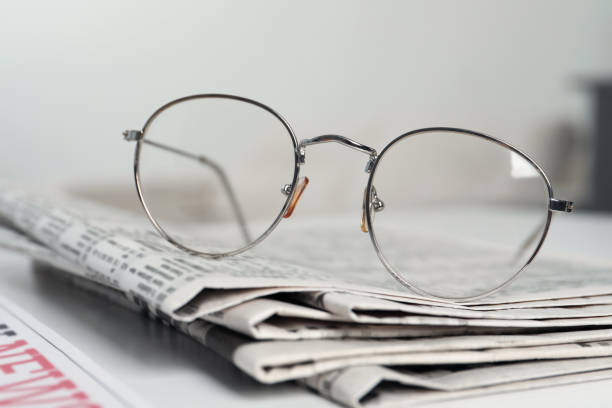istock Stack of newspapers and glasses on white table indoors, closeup 1445392973