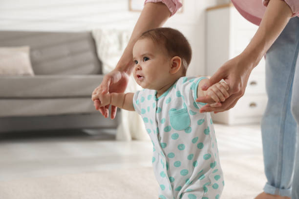 istock Mother supporting her baby daughter while she learning to walk at home 1445396687