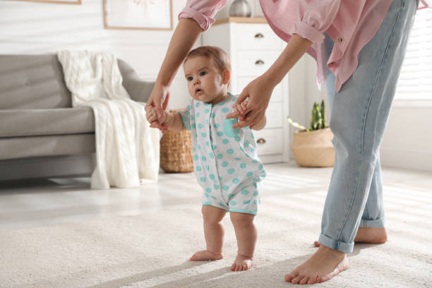 istock Mother supporting her baby daughter while she learning to walk at home 1445396962