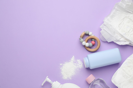 Flat lay composition with dusting powder and other baby care products on violet background, space for text
