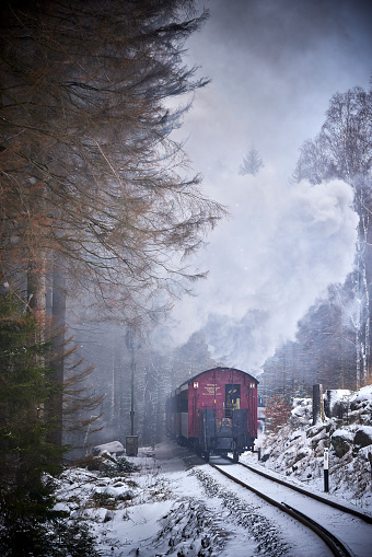 Historical steam train running full speed to Brocken Mountain in Harz region. The sky is grey, it is snowing, there is snow on the trees and the steam is coming out of the chimney.