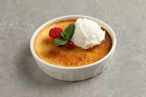 Delicious creme brulee with scoop of ice cream, fresh berries and mint on light grey table