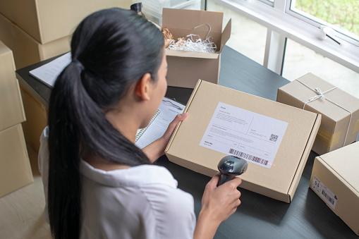 Asian woman business owner scanning barcode on delivery parcel.
